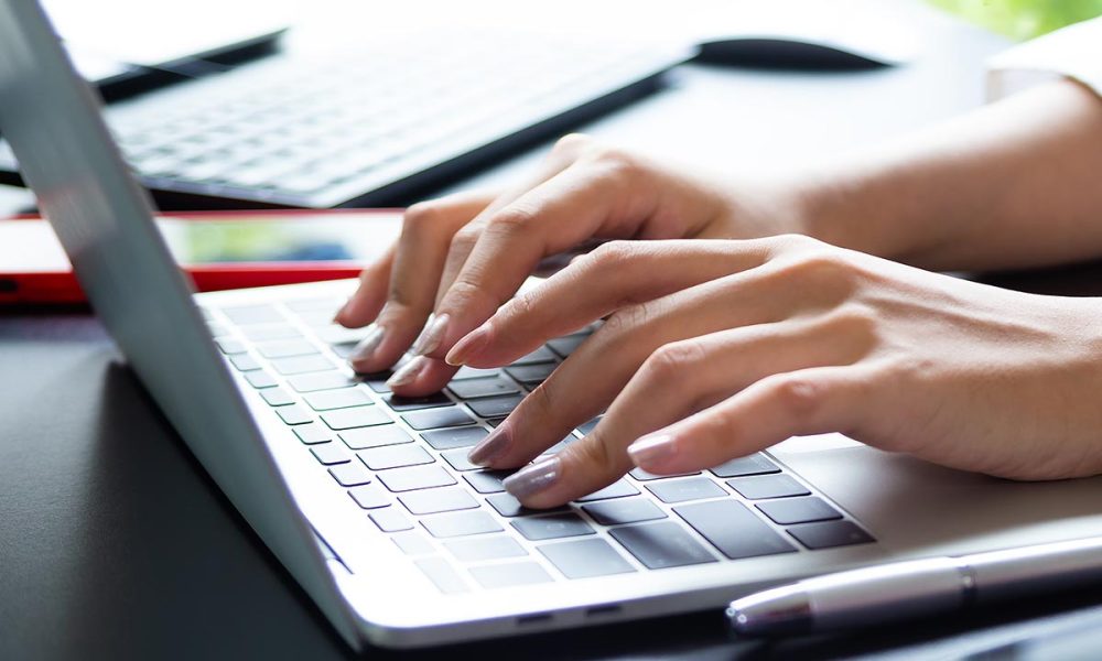 Close up hand of female typing on keyboard of laptop on table, working with technology device in modern office